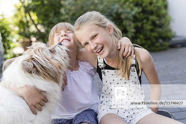 Zwei glückliche Schwestern kuscheln mit Hund im Hof