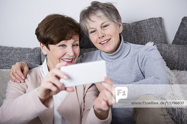 Zwei ältere Frauen  die auf der Couch sitzen und Selfies nehmen.