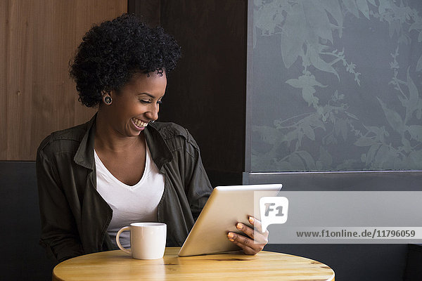Laughing young woman sitting in a coffee shop looking at tablet