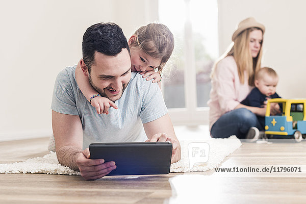 Vater und Tochter mit Tablette im neuen Zuhause mit Frau und Baby im Hintergrund