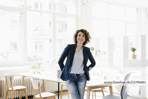 Businesswoman in office sitting on desk  looking confident
