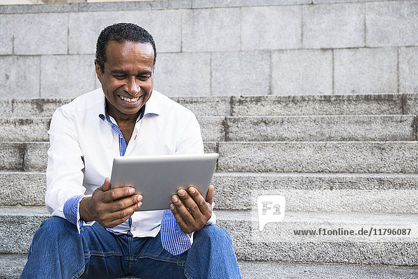 Portrait of smiling man sitting on stairs looking at tablet