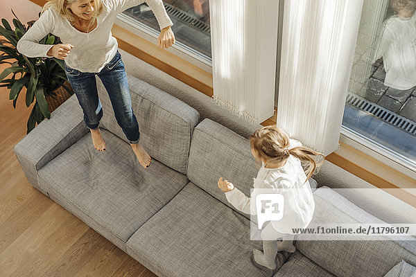 Reife Frau und Mädchen zu Hause auf der Couch hüpfend