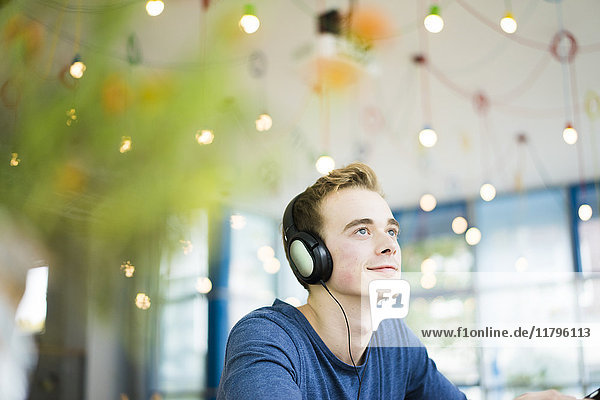 Porträt eines lächelnden jungen Mannes beim Musikhören mit Kopfhörern im Café