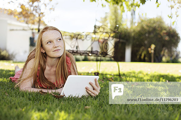 Grl with long red hair lying in grass with tablet