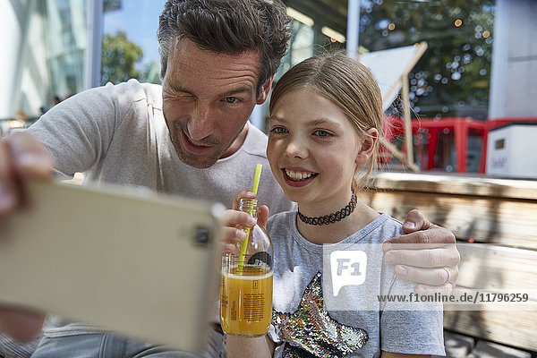 Verspielter Vater und Tochter beim Selfie in einem Outdoor-Café