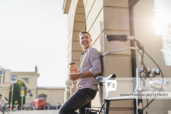 Lächelnder Mann mit Fahrrad und Kaffee zum Mitnehmen in der Stadt