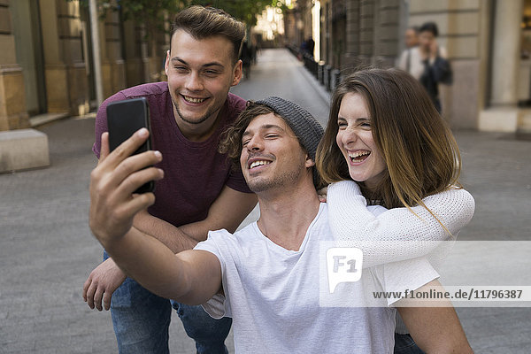 Three happy friends taking a cell phone selfie in the city