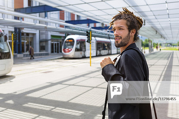 Porträt eines jungen Geschäftsmannes mit Rastalocken am Bahnhof