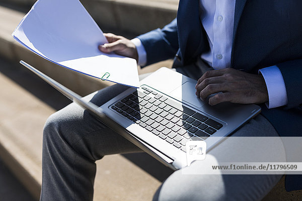 Businessman sitting on stairs with laptop and documents