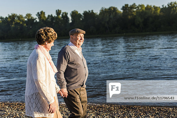 Glückliches Seniorenpaar  das Hand in Hand am Flussufer geht.