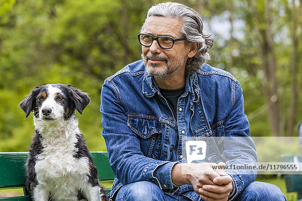 Portrait of man with grey hair and beard sitting beside his dog on a bench