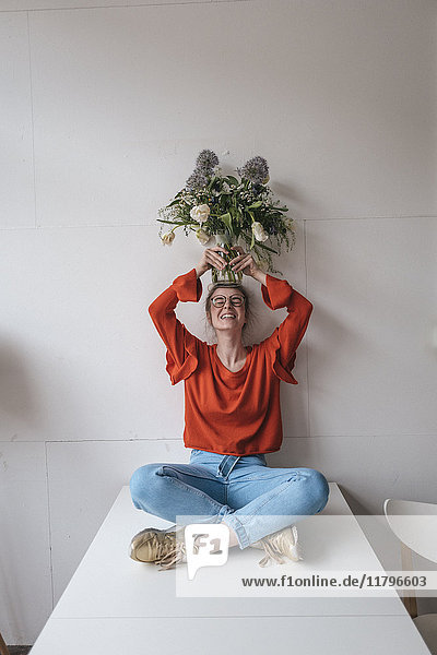 Junge Frau auf dem Tisch sitzend mit Blumenvase