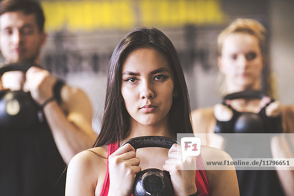 Selbstbewusste junge Frau mit Trainingspartnern beim Heben von Kettlebell im Fitnessstudio