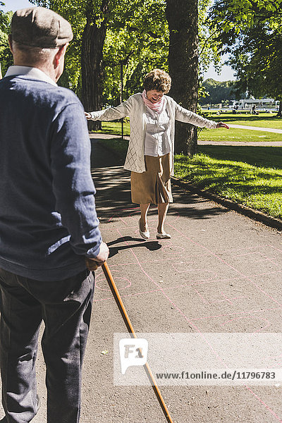 Senior woman playing hopscotch while husband watching her