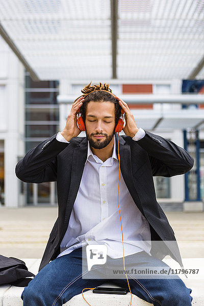Portrait eines jungen Geschäftsmannes mit Dreadlocks beim Musikhören mit Kopfhörer und Handy