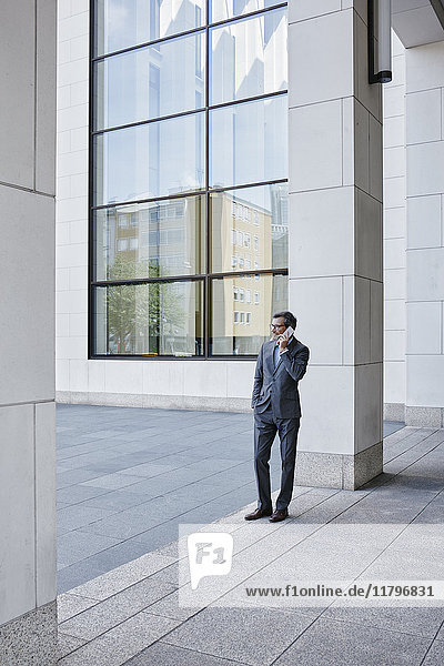 Erwachsener Geschäftsmann am Handy vor dem Bürogebäude