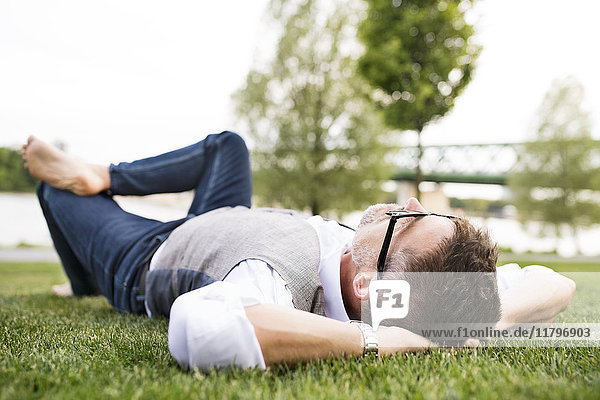 Mature businessman in the city park lying on grass
