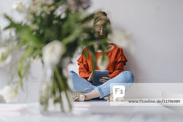 Young woman sitting on table using tablet covered by flowers