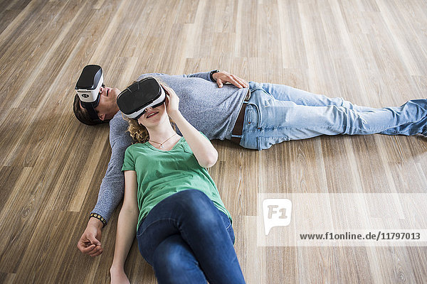 Young couple lying on floor in empty apartment wearing VR glasses