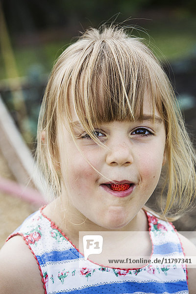 Lächelndes Mädchen isst eine Erdbeere und schaut in die Kamera.
