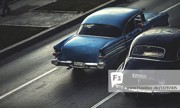 Hochwinkelaufnahme von zwei klassischen Autos aus den 1950er Jahren  die auf einer Straße fahren.