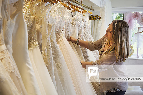 Eine Verkäuferin in einem Brautkleidergeschäft  die durch die in den Schienen hängenden Kleider blickt.