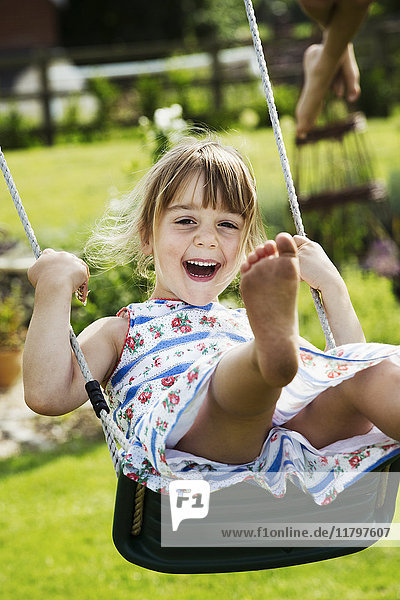 Lächelndes Mädchen im Sonnenkleid auf einer Schaukel in einem Garten.
