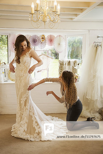 Eine Schneiderin nimmt ein Hochzeitskleid in Empfang  steckt es an und passt es der Kundin  einer jungen Frau  an. Eine Braut  die ihr Kleid in einem Fachgeschäft auswählt.