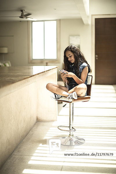 Ein Mädchen sitzt an einem Küchentresen und schaut auf den Bildschirm eines Mobiltelefons.