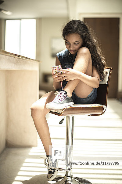 A girl sitting at a kitchen counter looking at a mobile phone screen.