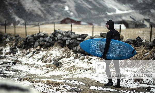 Ein Surfer in einem Neoprenanzug und mit einem Surfbrett  der an einem verschneiten Strand entlangläuft.