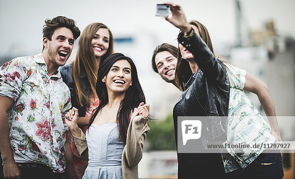 A group of five young people standing on a rooftop posing for a selfie.