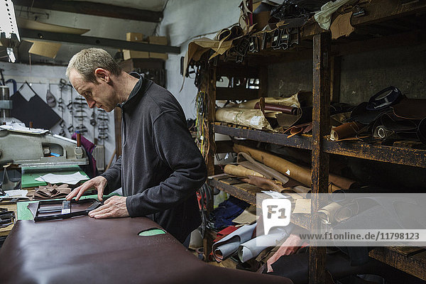 Man standing in a shoemaker's workshop  cutting brown leather.