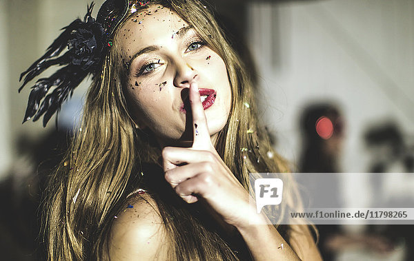 Junge Frau mit paillettenbesetzter Gesichtsmaske mit dem Finger auf dem Mund.