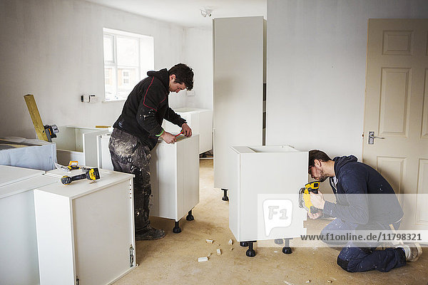 Zwei Bauarbeiter  die weiße Kücheneinheiten bauen.