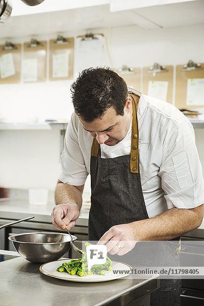 Chef standing in the kitchen in a small hotel  plating up a dish of vegetables.