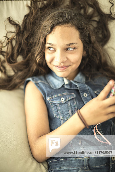 Ein Mädchen  das sich hinlegt  ein Mobiltelefon in der Hand hält und lächelt.