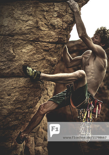 Bergsteiger mit nackter Brust  der mit Karabinerhaken und Seil eine Felsformation erklimmt.