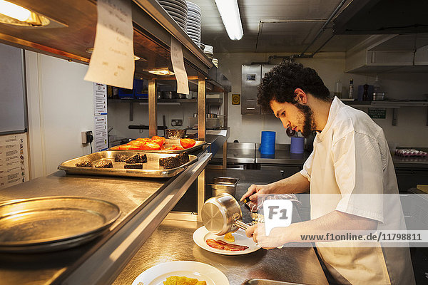 Chefkoch  der in einer Restaurantküche an einer Theke steht  eine Soßenpfanne hält und Essen plattiert.
