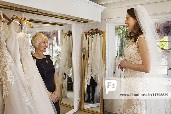 Eine Frau  eine zukünftige Braut  probiert mit Hilfe einer Verkäuferin in einem Brautkleidergeschäft Kleider an.