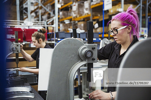 A young woman with pink hair  a female factory worker using a hole punching machine  working to assemble a bicycle in a factory.