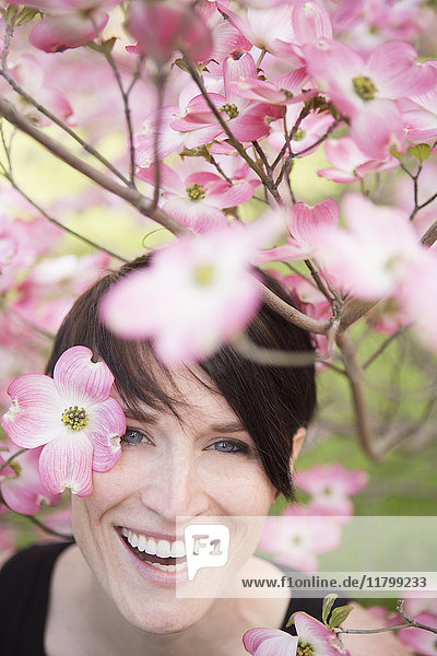 Eine Frau schaut durch die blühenden Zweige eines Baumes und lächelt.