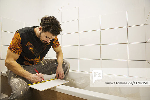 Ein Bauarbeiter  Fliesenleger  der in einem Badezimmer arbeitet und eine Fliese mit einem Bleistift markiert.