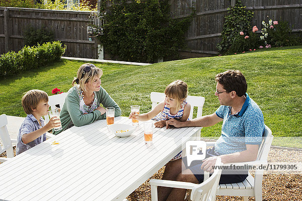 Eine Familie,  die um einen Gartentisch sitzt,  Eltern und zwei Kinder,  ein Junge und ein Mädchen.