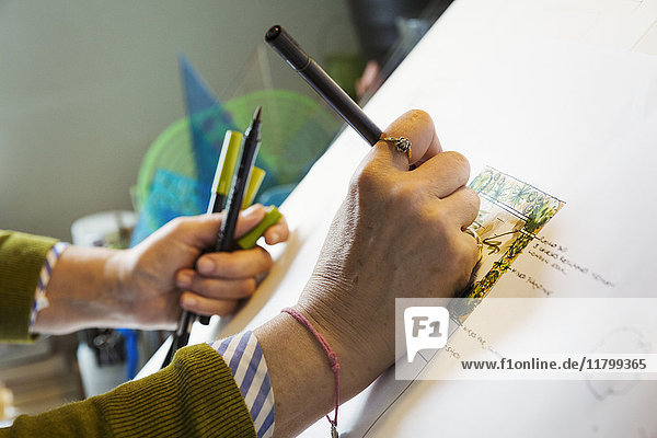 Nahaufnahme einer Frau  die an einem Zeichenbrett sitzt und mit einem feinen Linienstift unter Verwendung einer Designvorlage zeichnet.
