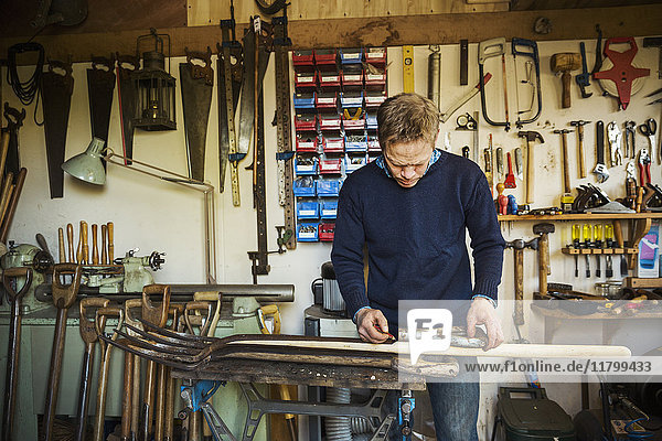 A man standing in a garden workshop  working on an old garden space  surrounded by tools. Equipment on the beams and bicycles hanging from the ceiling.