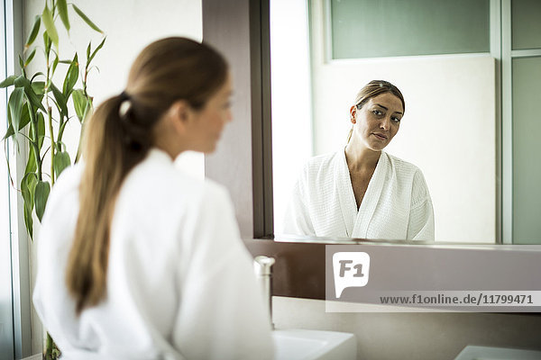 A woman standing in front of a bathroom mirror and looking at her reflection.