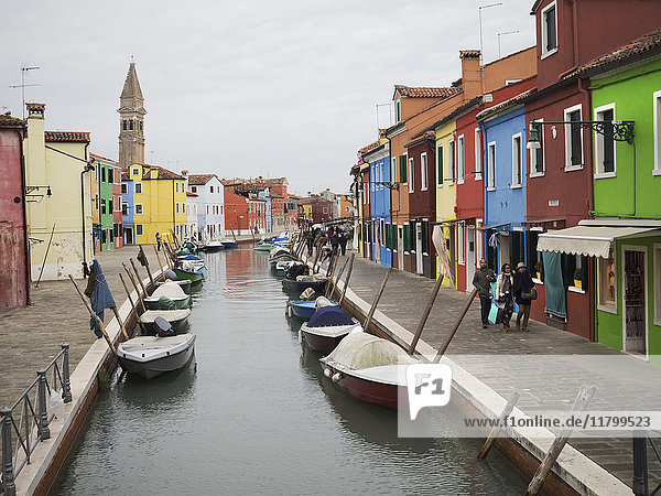 Venedig. Ein schmaler Kanal mit festgemachten Booten und einer Terrasse mit bunt bemalten Hausfassaden.