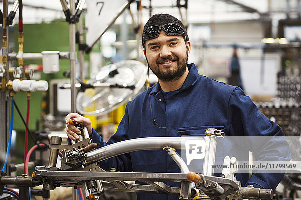 Männlicher Fabrikfacharbeiter mit einem teilweise montierten Fahrradrahmen in einer Fabrik.